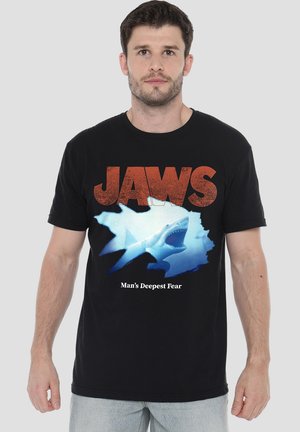 Black cotton t-shirt featuring "JAWS" in bold red lettering, a graphic of a shark in blue tones, and the text "Man's Deepest Fear" in white.