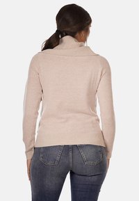 Maglione lavorato a maglia beige con colletto alto, design aderente e orlo a coste. Il tessuto sembra morbido, con maniche lunghe e silhouette rilassata.