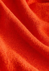 Helles orange Wollgewebe mit einer weichen, strukturierten Oberfläche. Das Material weist subtile Variationen in der Textur und Farbtiefe auf.