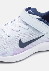 Białe i fioletowe dziecięce sneakersy z granatowymi akcentami, rzepem, sznurowadłami oraz czarnym logo Nike z boku.