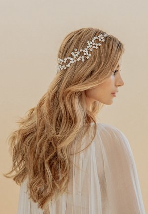 Cerchietto floreale con fiori bianchi su un filo d'argento, indossato in capelli lunghi e mossi biondi, su uno sfondo neutro. Il tessuto trasparente è visibile.