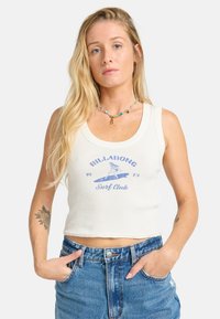 Hvid bomulds crop tank top med blå grafisk tekst "BILLABONG Surf Club" og surfbræt design. Kombineret med højtaljede denim shorts.