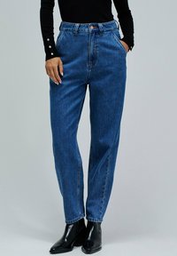 Jeans de mezclilla azul de talle alto con un corte holgado, que cuentan con un cierre de botón, dos bolsillos laterales y un ligero desgaste a lo largo de los muslos.