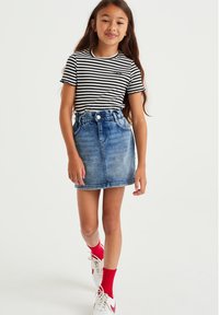 Camiseta de manga corta a rayas en blanco y negro combinada con una falda de mezclilla azul clara. Zapatillas deportivas blancas con acentos rojos y calcetines rojos.