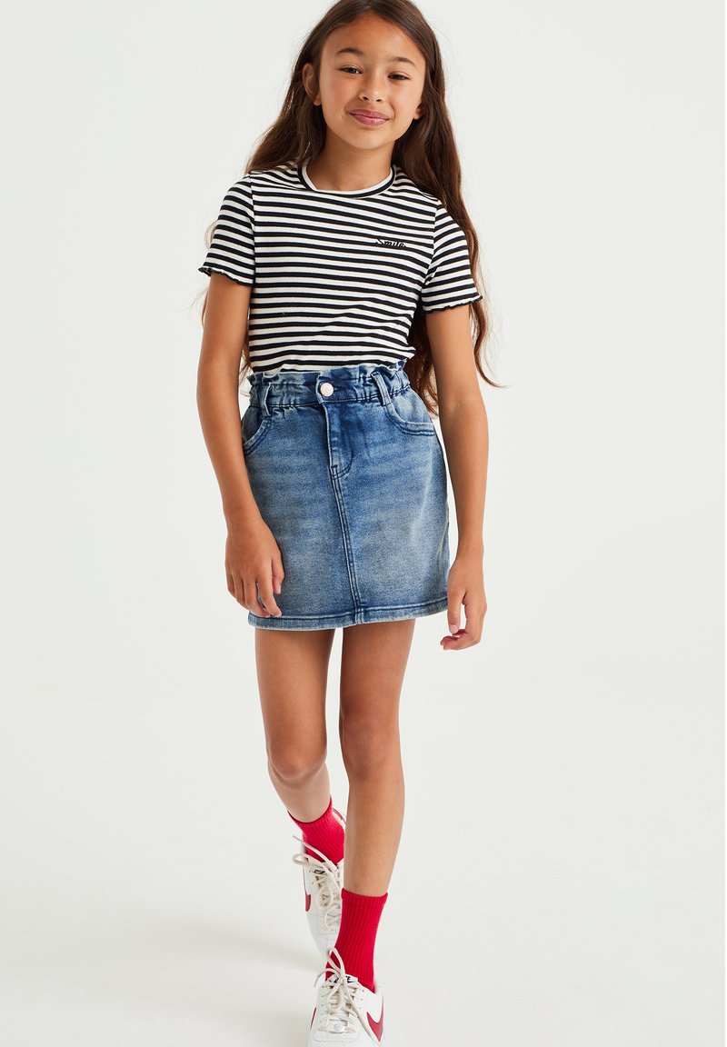 Camiseta de manga corta a rayas en blanco y negro combinada con una falda de mezclilla azul clara. Zapatillas deportivas blancas con acentos rojos y calcetines rojos.