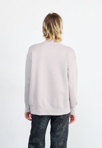 Lys grå sweatshirt med rund hals og dropped shoulders. Har ribbede mansjetter og kant, kombinert med mørke mønstrede bukser.