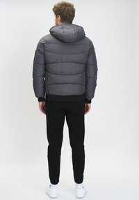 Siva puffer jakna s kapuljačom, s ušivenim dijelovima i rebrastim donjim dijelom. U kombinaciji s crnim tapered hlačama i bijelim tenisicama.