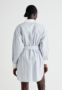 Gaiši zils svītrains kleitas krekls ar baltām svītrām. Iespējas: garas piedurknes, josta viduklī un apkakle. Kroku dizains aizmugurē.