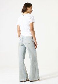 Camiseta blanca de manga corta con escote redondo y un pequeño detalle en la parte posterior, combinada con unos vaqueros acampanados de color azul claro que cuentan con bolsillos en la parte trasera.