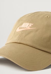 Bežs kokvilnas beisbola cepure ar teksturētu audumu, izliekts vizieris un izceltā rozā izšūtā Nike logo priekšpusē.