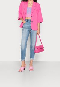 Růžový oversized blazer, modrý zkrácený pletený top, světlé džíny a růžové sandály na jehlovém podpatku. Ladící růžová texturovaná kabelka.