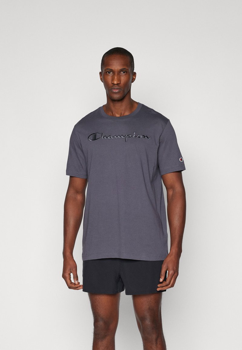 Graues Baumwoll-T-Shirt mit kurzen Ärmeln. Verfügt über ein schwarzes gesticktes "Champion"-Logo auf der Brust und ein kleines Logo auf dem Ärmel.