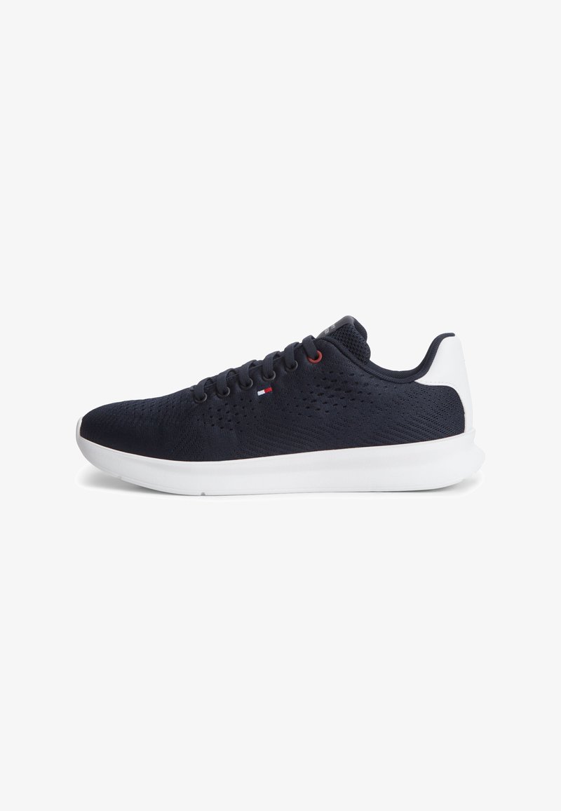 Baskets basses noires avec semelle et talon blancs, tige en maille respirante, lacets noirs et petit détail drapeau rouge, blanc et bleu sur le côté.