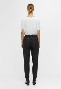 Pantalons noirs au design fuselé et à taille élastique, fabriqués dans un textile lisse. Associés à un t-shirt blanc pour un contraste.