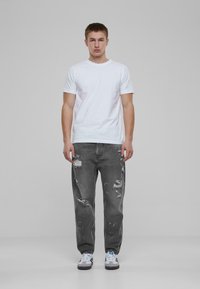 Camisa de algodón blanca y jeans grises desgastados con rasgaduras y manchas de pintura; modelo con zapatillas blancas con acentos negros.