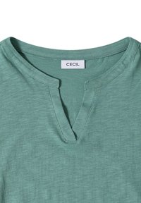 Světle zelené tričko s kulatým výstřihem s výřezem a viditelným švem kolem límce, uvnitř s etiketou značky "CECIL".