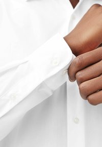 Chemise en coton blanche avec une texture lisse, dotée d'un poignet à bouton et d'un col standard. Les boutons sont de couleur crème.