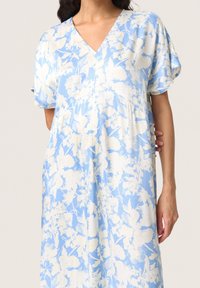 Ljusblå klänning med vitt blommönster. Har V-hals, korta ärmar och en lös passform med en samlad midja. Slät tygtextur.