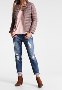 Brun polstret jakke med rund hals, lys pink top, slidte blå jeans og brune ankelstøvler med blokhæl.