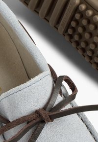 Shoe din suede albastru deschis cu o suprafață texturată, șireturi maro și talpă din cauciuc cu puncte de priză rotunde.