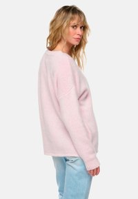 Pull surdimensionné rose clair avec un col rond, texture tricotée et épaules tombantes, associé à un jean bleu clair.