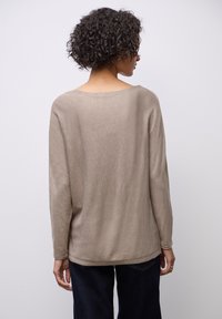 Maglione beige a maniche lunghe con scollatura ampia e taglio rilassato, realizzato in un materiale morbido e con una consistenza liscia. Vista posteriore, indossato con pantaloni scuri.