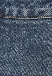 Tumši zila džinsa auduma virsma ar smalku tekstūru, kurā ir izlīdzena auduma struktūra un redzamas šuves detaļas gar augšējo malu.