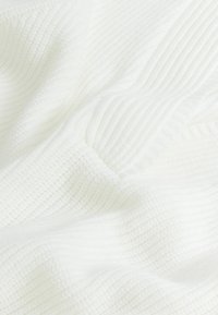 Rakenteeltaan valkoinen kangas, jossa on pehmeä, uritettu kuvio, luoden lämpimän ja kutsuvan ilmeen. Sileä pinta, jossa on lempeitä poimuja.