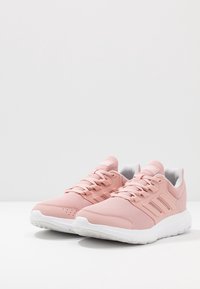 Zapatillas deportivas rosas con parte superior de malla, suela de goma blanca y tres franjas blancas a los lados. Diseño con cordones, con collar y lengüeta acolchados.