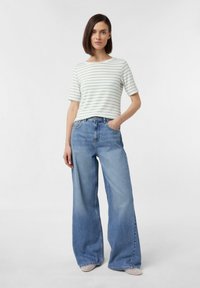 Pasiasta, dopasowana koszulka w jasnym zielonym i białym kolorze, zestawiona z szerokimi niebieskimi dżinsami. Dżinsy mają wysoki stan i klasyczny pięciokołnierzowy fason.