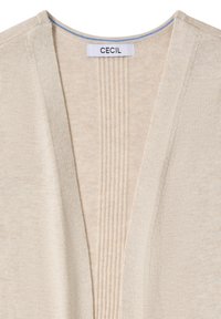 Cardigan tricoté beige avec des détails côtelés au niveau de l'encolure et une étiquette blanche avec le texte "CECIL" cousue à l'intérieur du col à l'arrière.