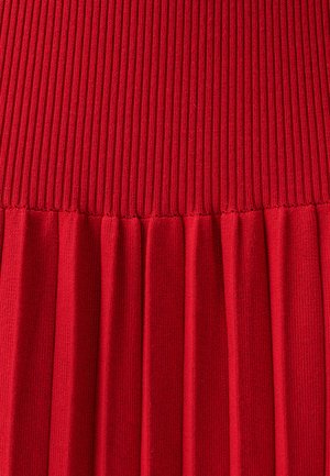 Rippene rotes Strickgewebe mit einer strukturierten Oberseite und einem plissierten unteren Abschnitt, der gleichmäßig verteilte, vertikale Rillen und Falten aufweist.