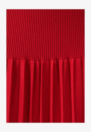 Ribbede røde strikkede stof med en struktureret overflade og en plisseret nederste del, der har jævnt fordelt, lodrette furer og folder.
