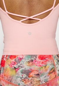 Top de desporto em rosa claro com alças cruzadas. Apresenta um padrão subtil e textura sem costuras. Combinado com leggings de padrão floral.