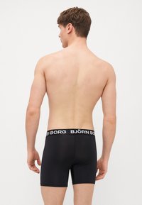 Črne bokserice z mekim pasom, ki vsebujejo belo "BJÖRN BORG" blagovno znamko. Gladka tekstura, udoben prileganje in dolžina do sredine stegna.