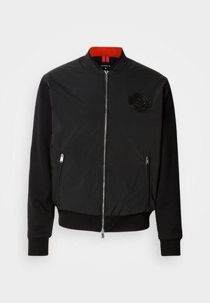 Melna bomber jakna ar sarkanu iekšējo apkakli, ar rāvējslēdzēju, sānu kabatām un teksturētu emblēmu uz krūtīm. Ribota piedurkņu un apakšmala.