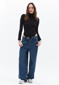 Schwarzer Langarm-Body, kombiniert mit lockeren, hellblauen Jeans mit hoher Taille, Knopfverschluss und weitem Bein.
