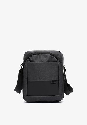 Šedá látková taška cez rameno so zipsom, ktorá má predné vrecko a čierny akcentový panel na spodnej strane. Súčasťou je nastaviteľný popruh.