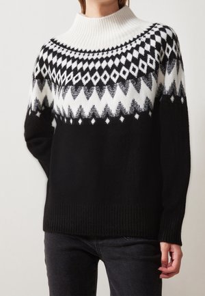 Pull en maille noir et blanc avec motif géométrique diamant et zigzag sur le haut de la poitrine et les épaules, associé à un jean foncé.
