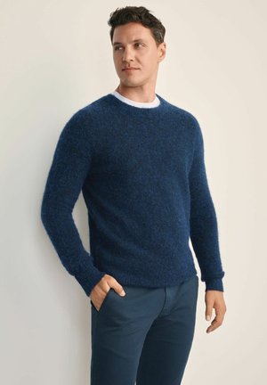 Granatowy wełniany sweter o teksturowanym, puszystym wykończeniu; okrągły dekolt; długie rękawy; stylizowany z ciemnymi spodniami; półdopasowany krój.