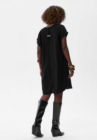 Czarna sukienka z krótkim rękawem, luźny krój, z szwem z tyłu i delikatną metką. Połączona z wyszkimi, błyszczącymi czarnymi botkami.