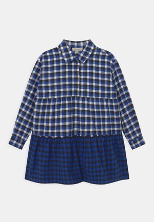 Robe chemise à carreaux bleus et noirs avec col, devant à boutons, manches longues et ourlet à volants superposés. Fabriquée en tissu léger.