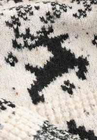 Gebreide stof met een zwart-wit rendierpatroon; zachte textuur met een pluizige uitstraling; lichtcrème achtergrond met donkere accenten.