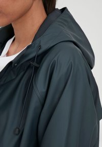 Donkergroene waterdichte jas met capuchon, voorzien van een gestructureerd oppervlak, verstelbare trekkoord en ritsluiting. Eenvoudig ontwerp.