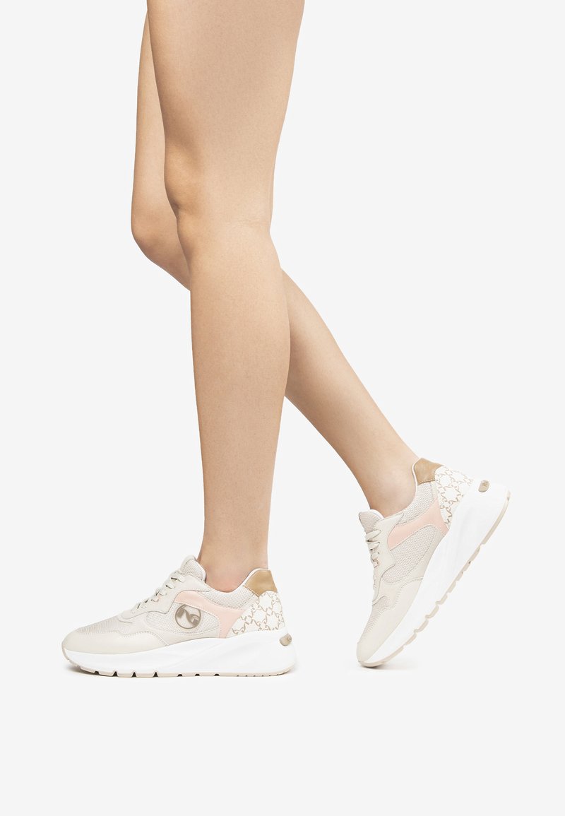 Deportivas en beige con detalles en rosa y dorado, que presentan un patrón texturizado en el talón y una suela blanca acolchada.