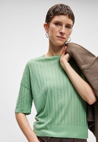 Ανοιχτό πράσινο κοντομάνικο πουλόβερ με υφασμάτινη, κατακόρυφη ριγέ σχέδιο. Διαθέτει στρογγυλή λαιμόκοψη και ελαφρώς στενή στη βάση.