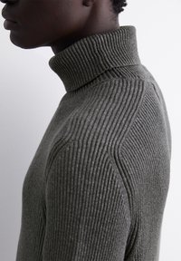 Dunkelgrün geripptes Rollkragensweatshirt mit hohem Kragen und strukturiertem Material. Mit eng anliegenden Ärmeln und einer schlanken Silhouette.
