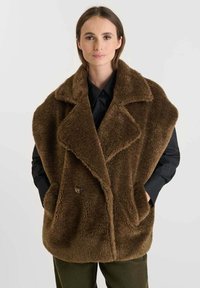 Bruine faux fur oversized jas met grote kraag, dubbelsluitende knopen en zijzakken. Draagt over een zwart shirt, met een gladde textuur.