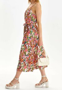 Värikäs kukkakuosis maxi-mekko, jossa on ohuet olkaimet, vyötä ympärille kiristävä vyötärö ja hulmuava helma. Valkoiset remmissandaalit korolla ja kerma värinen käsilaukku.