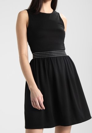 Schwarzes ärmelloses Kleid mit einem enganliegenden Oberteil und einem gerafften Rock, ausgestattet mit einem mit Nieten besetzten Gürtel an der Taille und einem glatten, weichen Stoff.